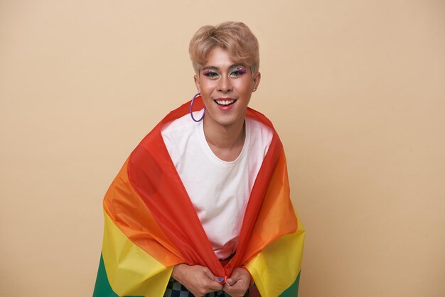 Молодежный азиатский трансгендер ЛГБТ с радужным флагом на плече изолирован на фоне обнаженного цвета