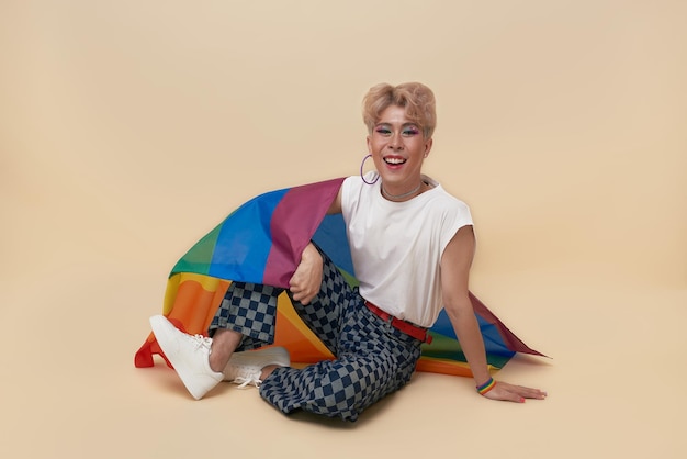 Transgender asiatico giovanile lgbt con bandiera arcobaleno sulla spalla isolata su sfondo color nudo