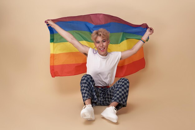 Youth asian transgender LGBT with Rainbow flag on shoulder isolated over nude color background