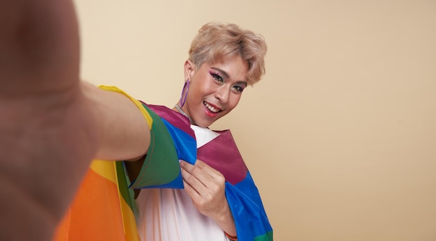 Youth asian transgender lgbt with rainbow flag on shoulder making selfie isolated over nude