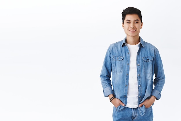 Free photo youth career headhunter and lifestyle concept portrait of smiling young healthy asian guy smiling hold hands in pockets casually standing over white background pleased making good investment