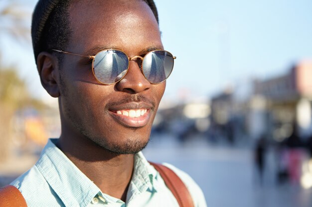 Free photo youth and happiness. people and lifestyle. close outdoor highly-detailed shot of attractive young african male with back smiling happily, enjoying good day and nice weather, walking on city streets