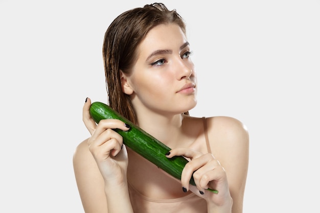 Youth secrets. Close up of beautiful young woman with cucumber on white background.