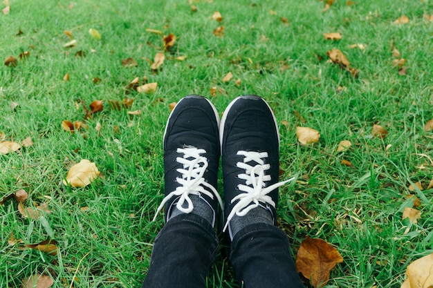 youth sneakers on girl legs on grass during sunny serene summer day.