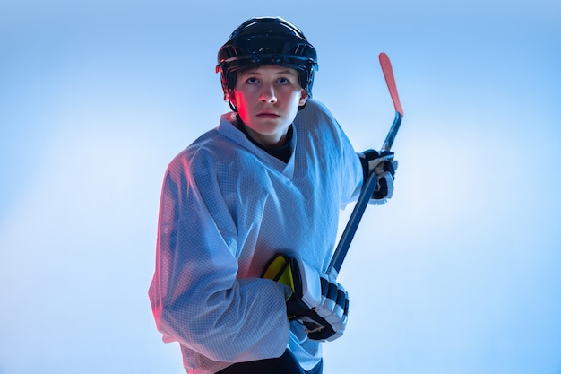 Gioventù. giovane giocatore di hockey maschio con il bastone sul muro bianco in luce al neon. sportivo che indossa attrezzature e pratica del casco. concetto di sport, stile di vita sano, movimento, movimento, azione.