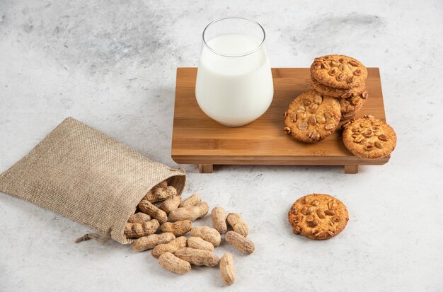 Yummy biscuits with honey and peanuts and glass of milk on wooden board. 