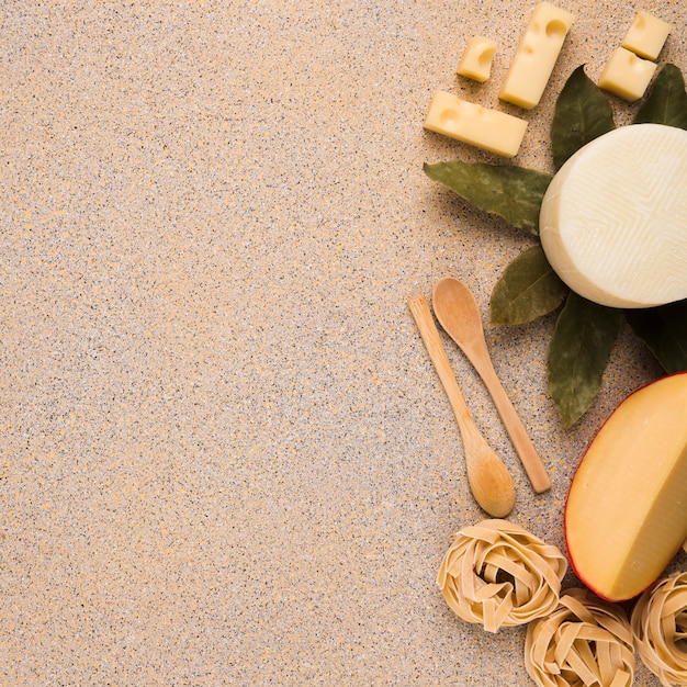 Бесплатное фото Вкусные свежие виды сыров с сырой пастой; лавровый лист и деревянная ложка на мраморной поверхности