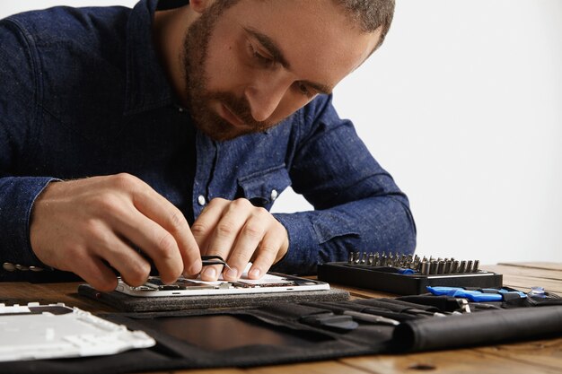 Yung bearded master looks inside disassembled electronic device while repairing it with tools