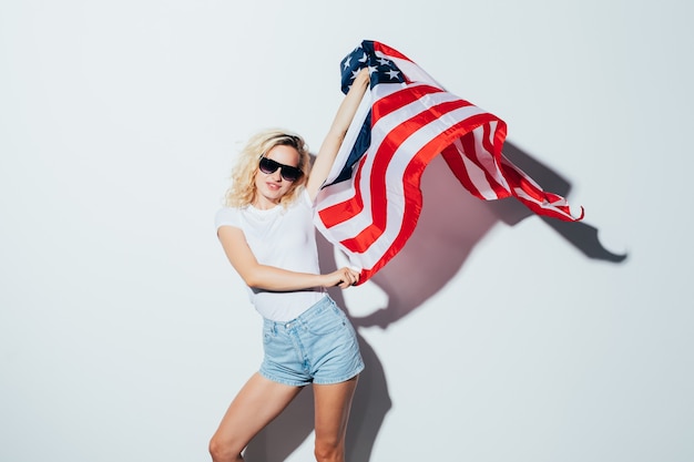 Yung caucasian blonde woman in sunglasses posing and waving USA flag, Independence Day Celebration