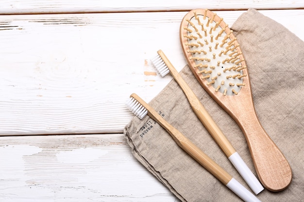 Zero waste concept with bathroom accessories on white wooden background. wooden hairbrush and two bamboo toothbrushes on a linen towel