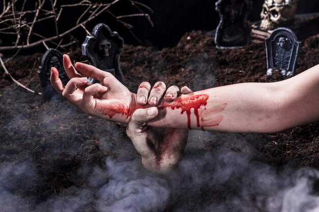 Zombie hand holding bloody woman arm at Halloween graveyard