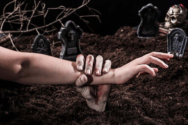 Zombie hand holding person arm at Halloween graveyard