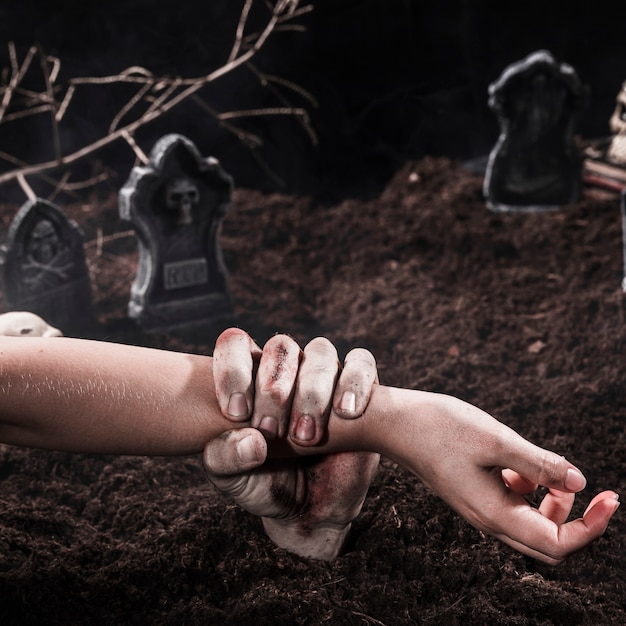 Zombie hand holding  person arm at Halloween graveyard