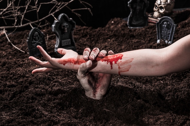 Zombie holding bloody female hand at Halloween graveyard