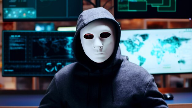 Zoom in shot cyber criminal wearing a white mask looking at the camera.
