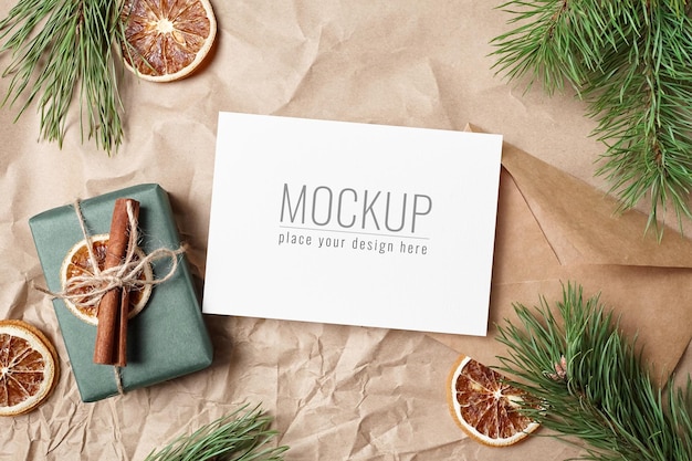 Christmas greeting card mockup with gift box, dry oranges and pine tree branches on craft paper