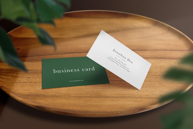 Чистый минимальный макет визитной карточки на деревянной тарелке и тени зеленых листьев. Premium Psd