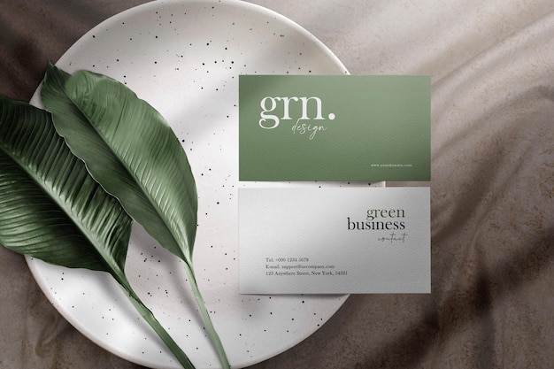 Clean minimal business card mockup on plate with leaves and fabric background