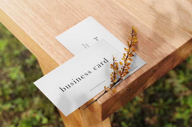 Clean minimal business card mockup on top wooden table with plant background. psd file.