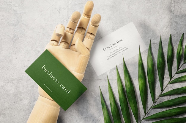 Clean minimal business card mockup on wooden hand and plant background. psd file.