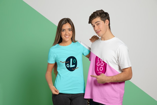 Front view of man and woman posing in t-shirts and pointing at them