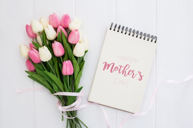 Happy mother's day mock up on notebook with pink and white tulips, on white wooden background