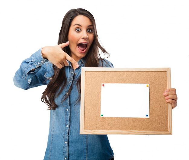 Joyful teenager pointing to a cork board with a blank paper