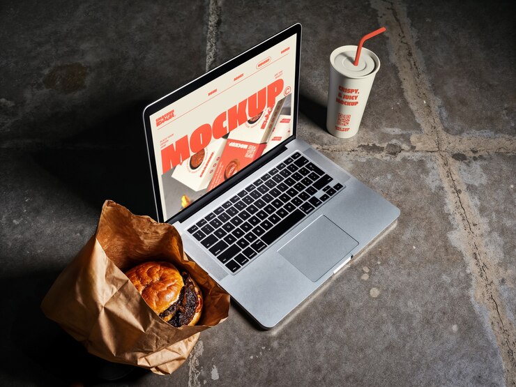 Free PSD laptop mockup with burger, drink, and food packaging.