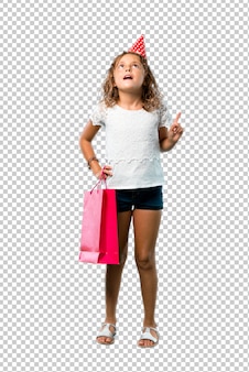 Маленькая девочка на вечеринке по случаю дня рождения держа мешок подарка стоя и думая идея