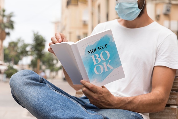 Man with mask on street reading book