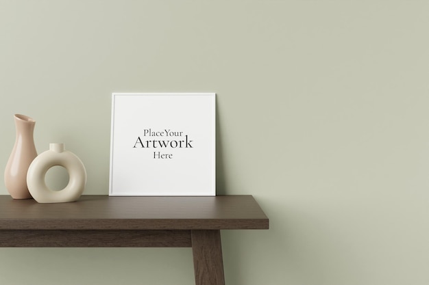 장식용 꽃병이 있는 방 벽에 기대어 있는 나무 테이블에 있는 미니멀하고 깨끗한 정사각형 흰색 포스터 또는 사진 프레임 모형