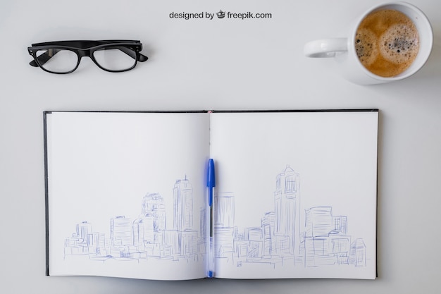 Open notebook with pen drawing, glasses and coffee