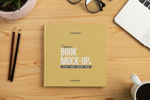 文房具と木製の机の上の正方形の本のモックアップ Premium Psd