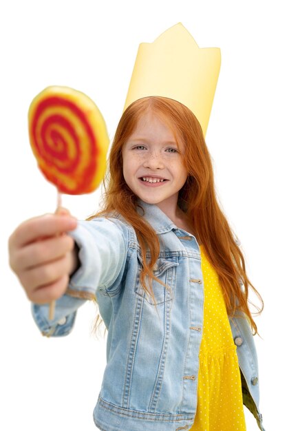 Studio portrait of young girl with paper crown and lollipop