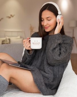 Woman listening to music on headphones while holding a mug mock-up Free Psd