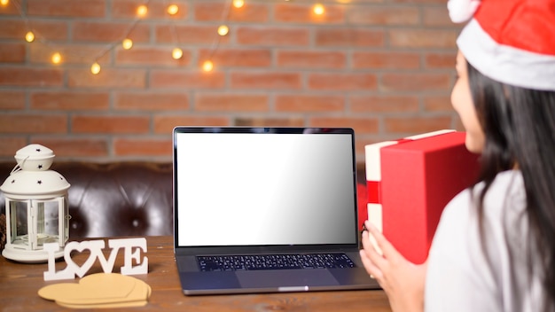 Young smiling woman wearing red santa claus hat making video call on laptop mockup