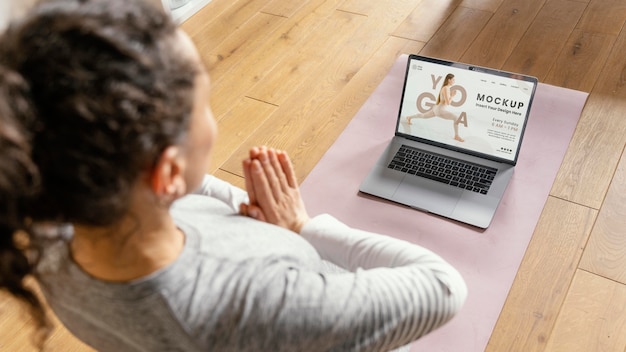 Giovane donna a casa che fa yoga con il computer portatile