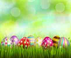 Free vector colorful painted easter eggs on green grass on blurred  with bokeh realistic