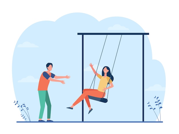 Happy young couple having fun on playground. Guy swinging girlfriend on swings