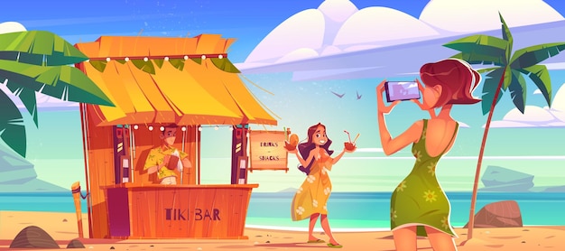 バーテンダーとティキ小屋バーの近くでカクテルを片手に写真撮影のためにビーチでポーズをとる女性