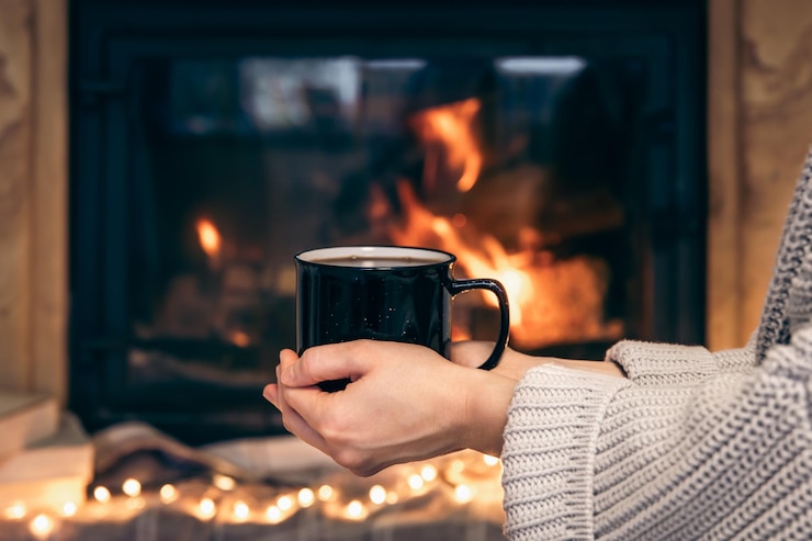 Gratis Foto a cup with a hot drink in female hands on a blurred fireplace background
