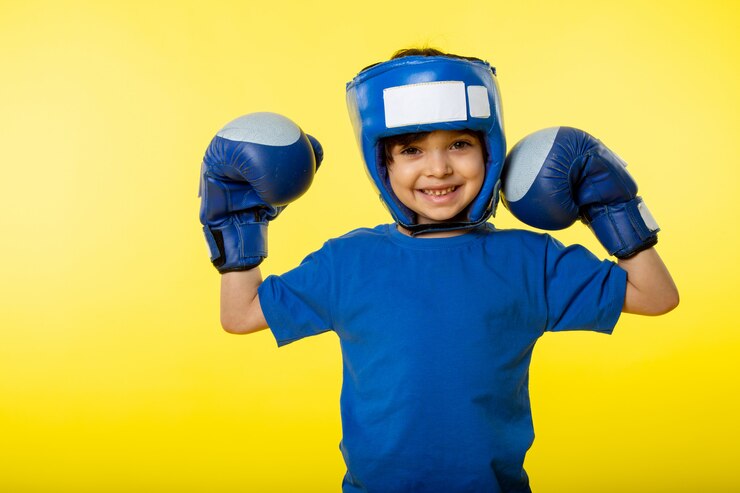 Gratis Foto a front view smiling cute boy in blue boxing gloves blue boxing helmet and in blue t-shirt on the yellow wall