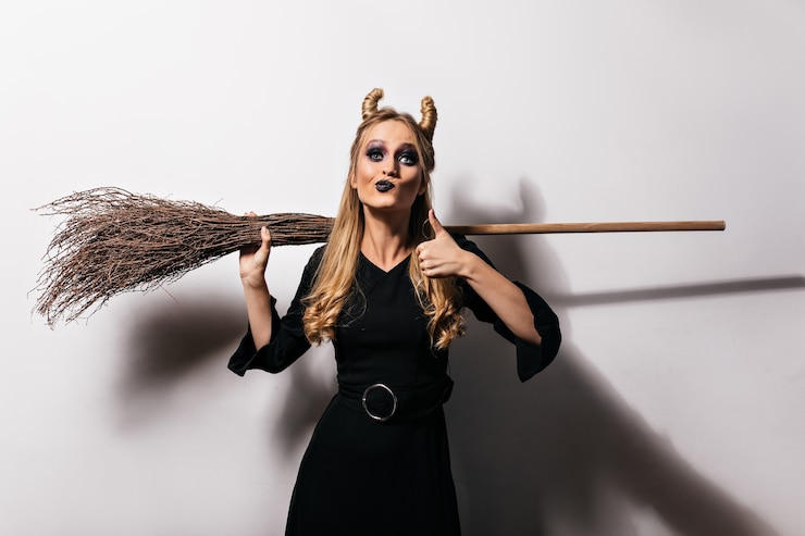 Gratis Foto adorable blonde witch enjoying halloween photoshoot. elegant vampire girl in long dress holding broom.