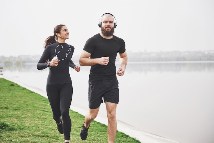 Gratis Foto couple jogging and running outdoors in park near the water. young bearded man and woman exercising together in morning