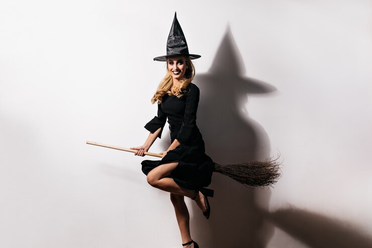 Gratis Foto ecstatic young woman in witch hat having fun in carnival. indoor photo of elegant caucasian girl sitting on magic broom.
