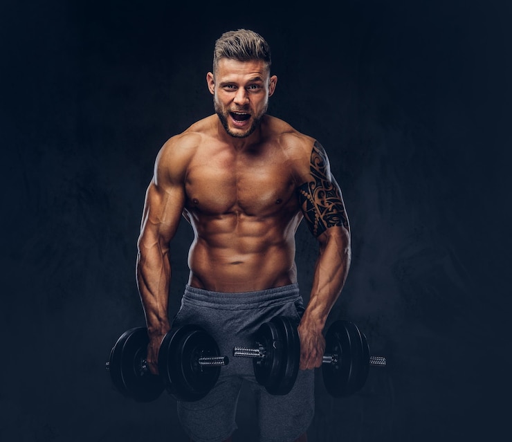 Gratis Foto funny stylish bodybuilder with a tattoo on his arm, doing the exercises with dumbbells. isolated on a dark background.