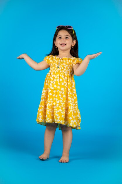 Happy cute baby girl fashionable yellow baby clothes posing studio on blue background