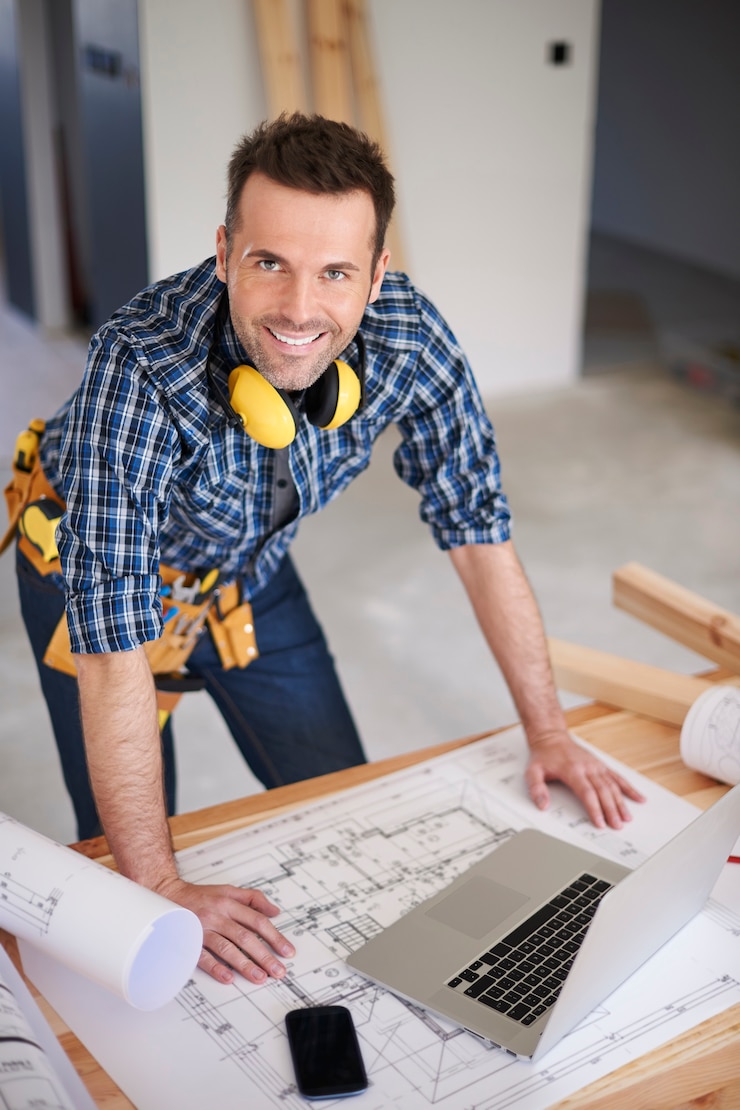 Gratis Foto smiling construction worker with plans and a laptop