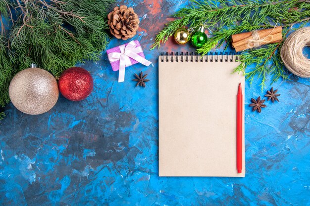 Top view red pencil on a notebook pine tree branches on blue surface with free space