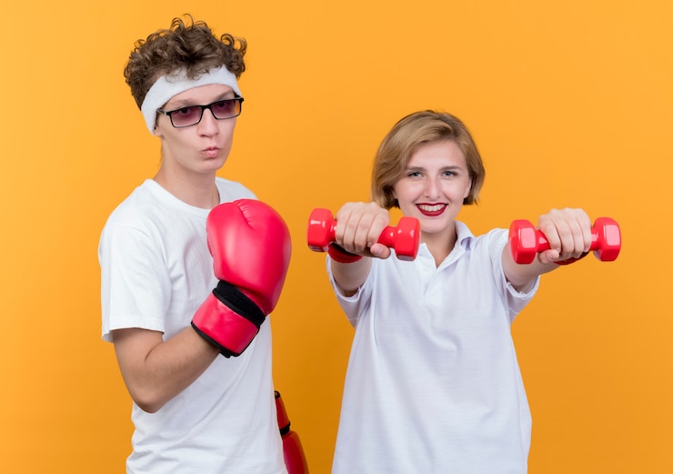 Gratis Foto young sporty couple woman with dumbbells next to her boyfriend with boxing gloves posing over orange